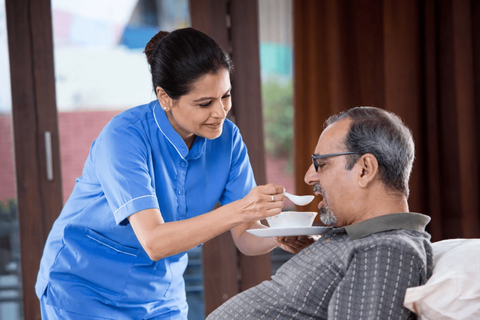 Caring nurse feeding elderly patient